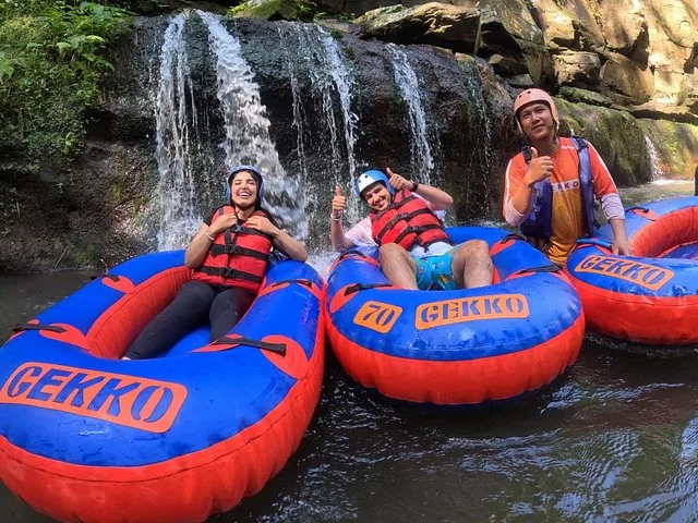 Three people relaxing in colorful tubes near a small waterfall on a river.