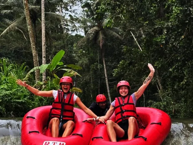 Dos mujeres riendo y saludando mientras descienden por una cascada en neumáticos rojos.